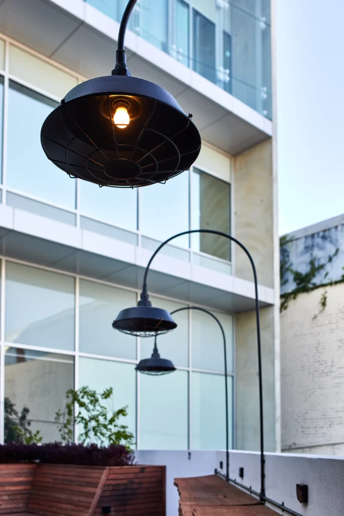 Close view of a black dish pendant light with a wire cage guard and warm lamp on a curved arm above an outdoor bar
