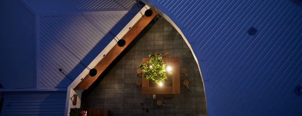 Night view of the Atwell Arcade alfresco courtyard from above, with a lit communal table, feature garden lighting and pendant lights along the beam