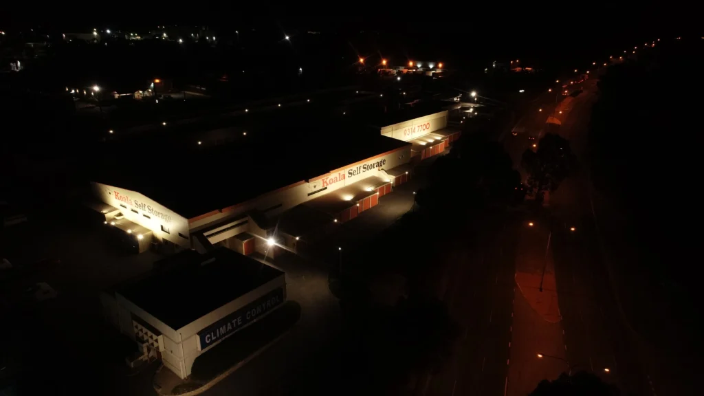 Aerial night view of a self storage facility with both signage faces evenly lit and the adjacent road left dark