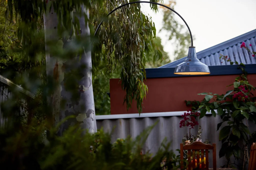 Curved steel arm carrying an outdoor pendant light arcing over a Fremantle courtyard against an evening sky