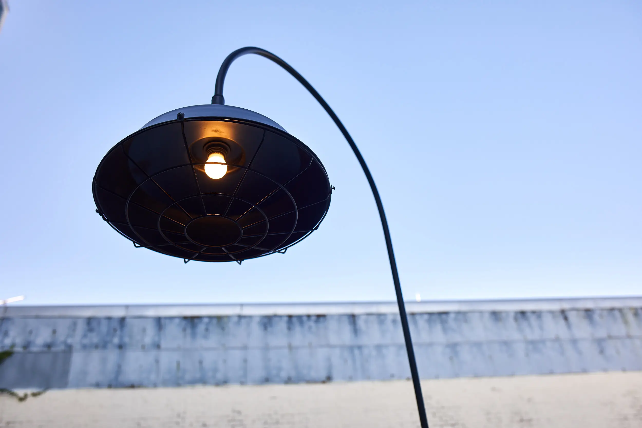 Single black gooseneck light fitting with a warm lamp curving against a clear evening sky