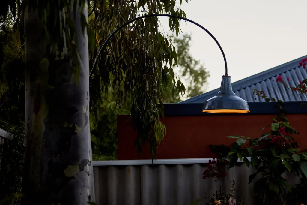 Recycled industrial pendant light on a curved arm silhouetted against a Fremantle sky above a red rendered wall