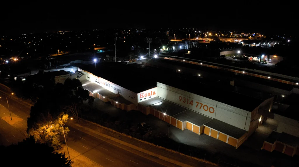 Rows of storage units lit by old floodlighting with bright glare points and dark sections between them