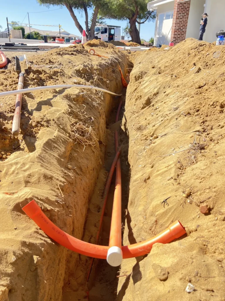 Orange electrical conduit with a sweeping bend and capped end laid in an open sand trench