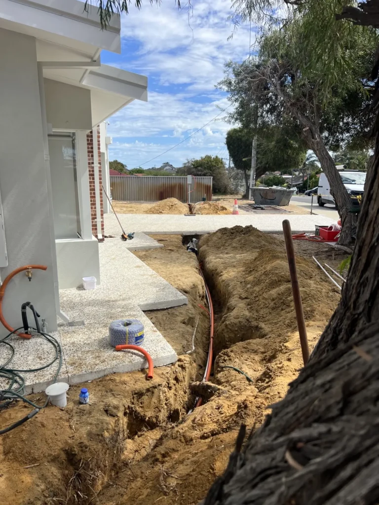 Open trench with orange electrical conduit running alongside a house on a Warwick subdivision
