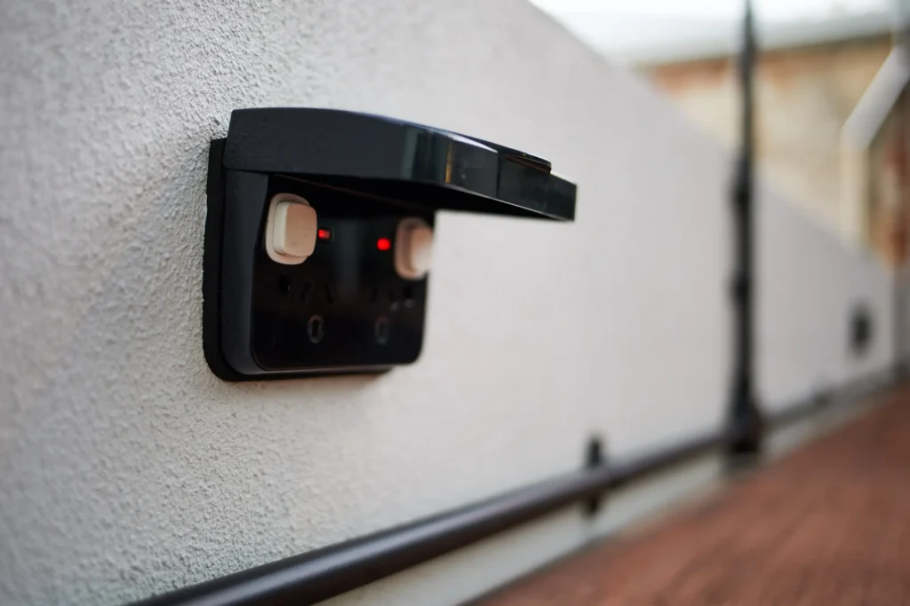Weatherproof double power point with a black hinged cover, surface mounted on a rendered courtyard wall with black conduit below